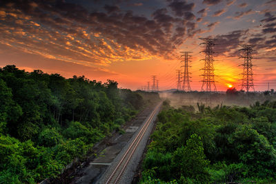 Railroad tracks amidst trees against sky during sunset