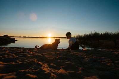 People sitting on shore against sky during sunset