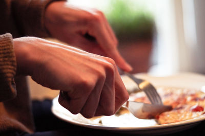 Midsection of person having food in plate with fork and knife on table