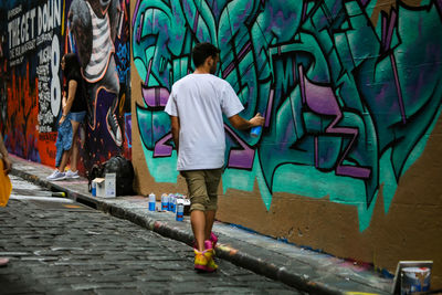 Full length rear view of man painting on graffiti wall