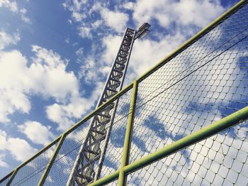 Low angle view of floodlight and chainlink fence against sky