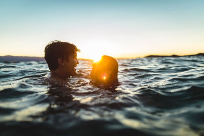 Young couple swimming in sea against sky