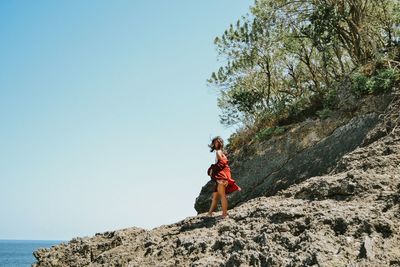 Side view of woman standing on rock at beach against clear sky