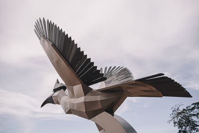 Low angle view of statue bird flying against sky