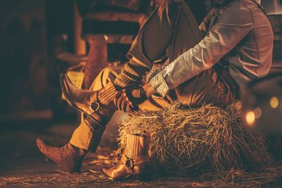 Low section of mid adult man wearing shoes while sitting on hay