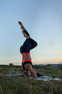 Full length of woman exercising on field against sky