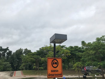 Road sign by trees against sky