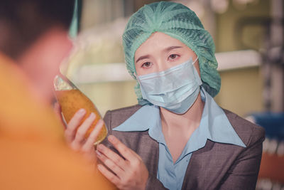 Close-up of woman wearing mask inspecting drink in factory