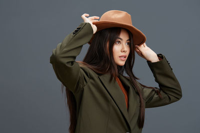 Portrait of young woman wearing hat standing against gray background
