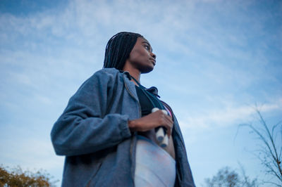 Side view of young woman looking away against sky