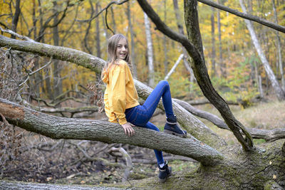 Portrait of smiling girl sitting on tree trunk in forest