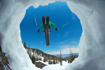 Low angle view of person skiing on snow covered field against blue sky