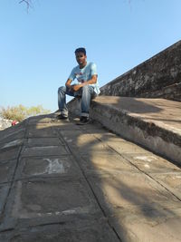 Man sitting on retaining wall against clear sky