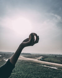 Cropped hand of woman holding crystal ball against sky