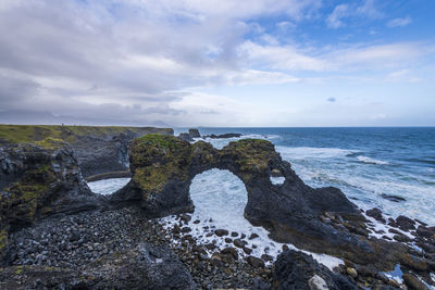 Seascape with natural arch and coastline mountains in distance, arnarstapi, iceland