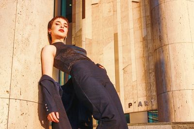 Young woman looking away while standing against wall