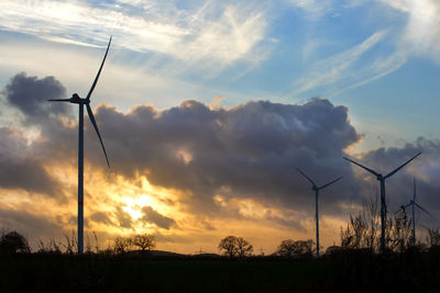 Low angle view of silhouette wind turbines on field against sky