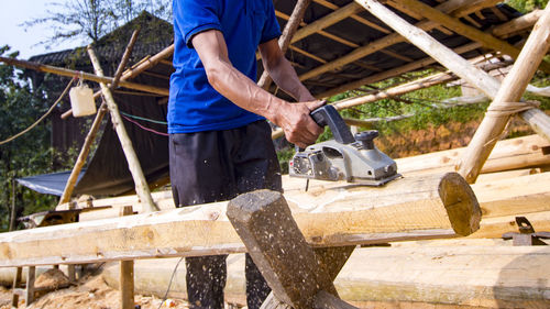 Midsection of male worker cutting log with circular saw at construction site