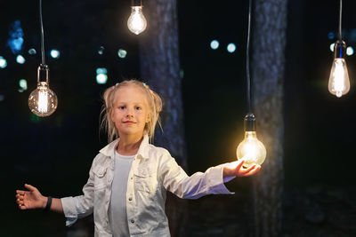 Portrait of smiling girl holding illuminated lights at night