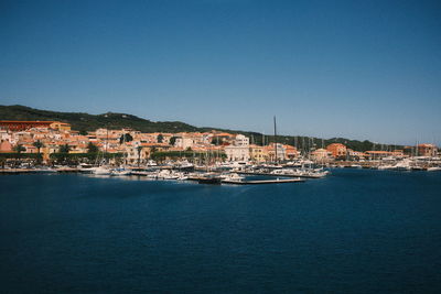 Buildings by sea against clear blue sky