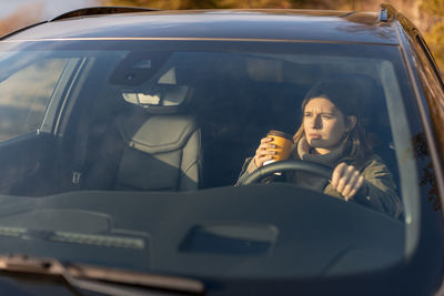 Young girl in the morning goes to work by car and drinking coffee. view through the windshield.