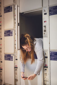 Young woman using phone in locker