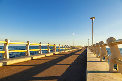 Empty road along calm sea against clear sky