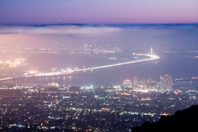 Aerial view of illuminated bay bridge and cityscape at night