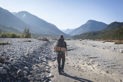 Hiker with backpack walking towards karwendel mountains, rissbach, vorderriss, bavaria, germany
