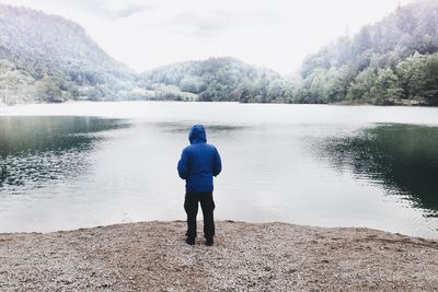 Rear view of man standing on lake against sky