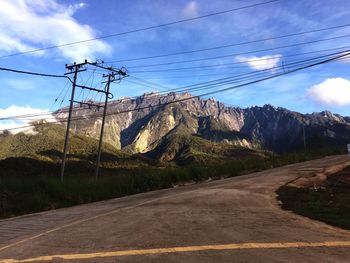 Road by electricity pylon against sky