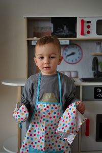 Cute little toddler with apron and glove standing in front of toy kitchen set