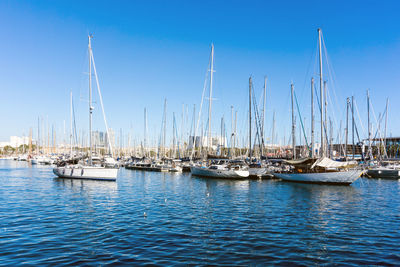 Sailboats moored in sea against clear blue sky