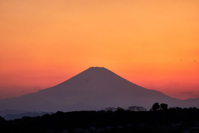 Scenic view of silhouette volcanic mountains against orange sky