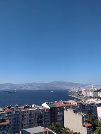 High angle view of city by sea against clear blue sky