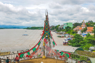View of amusement park by buildings against cloudy sky