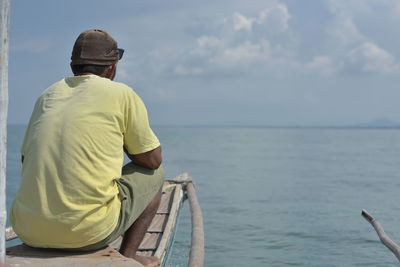 Rear view of man sitting on boat in sea against sky