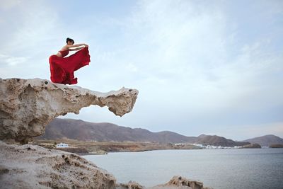 Man on rock by sea against sky