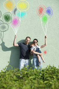 Full length photo of a smiling young couple with a baby and balloons