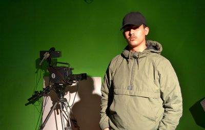 Portrait of man standing by movie camera against green wall