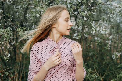 Blonde girl on a spring walk in the garden with cherry blossoms. female portrait, close-up. 