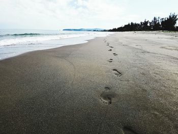 Footprints on sand at beach against sky