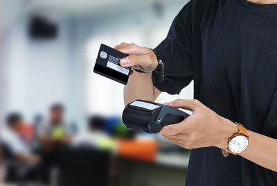 Young asian student holding an electronic data capture (edc) machine and ready to swipe credit card or debit card for pay over beautiful blur background