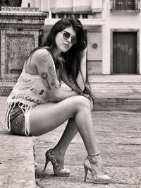 Side view of young woman sitting on retaining wall in city