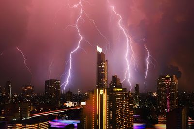 Lightning over illuminated buildings in city against sky at night