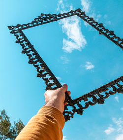 Low angle view of person holding chain against sky