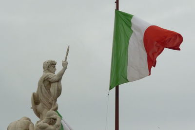 Low angle view of statue and italian flag against clear sky