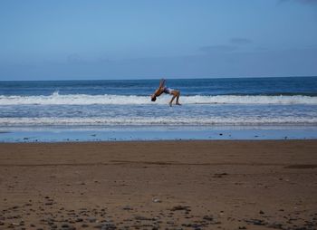 Man jumping at beach against sky