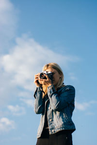 Low angle view of woman photographing with camera against sky