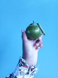 Close-up of woman holding apple against blue wall